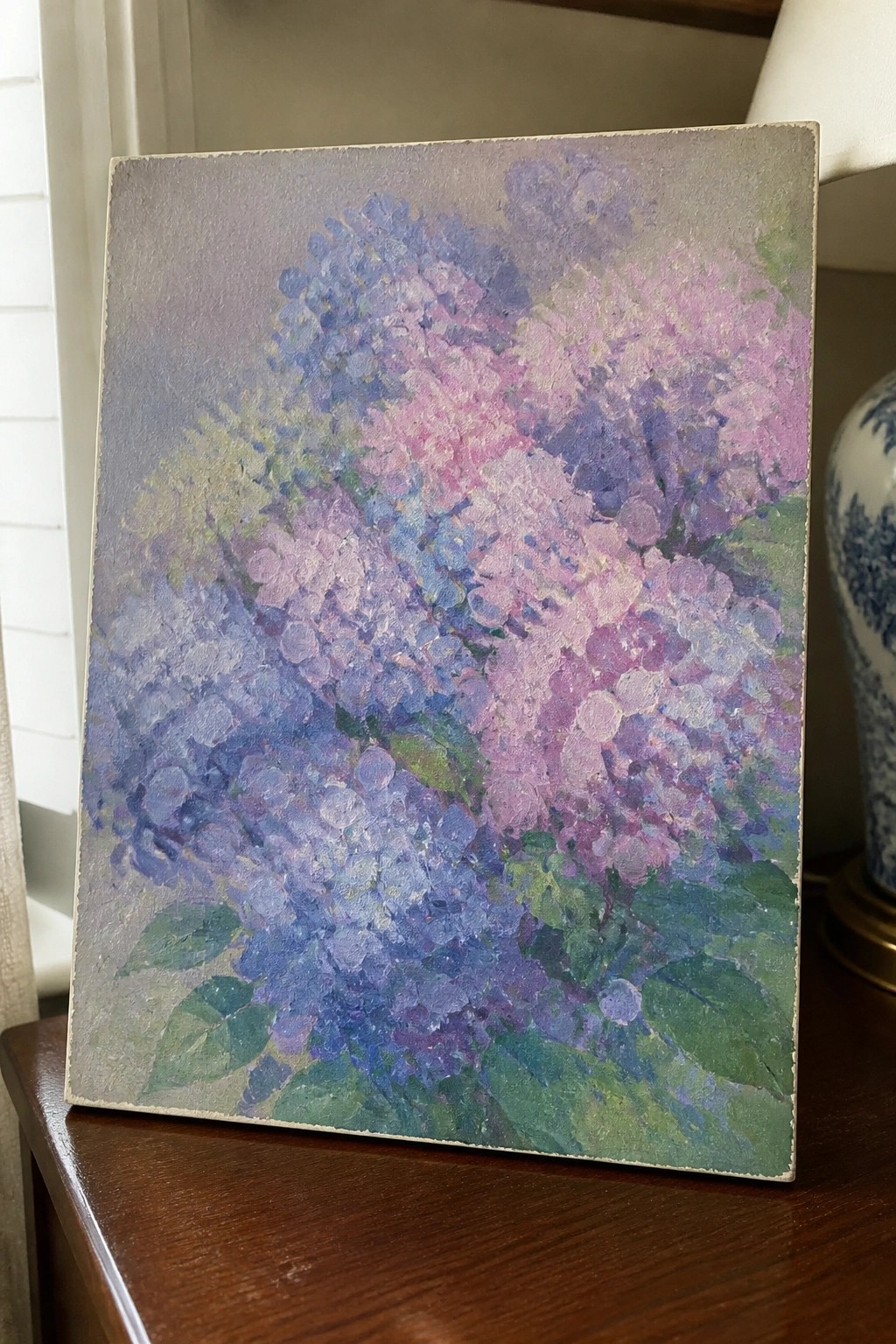 Impressionistic painting of blue, purple, and pink hydrangeas with green leaves