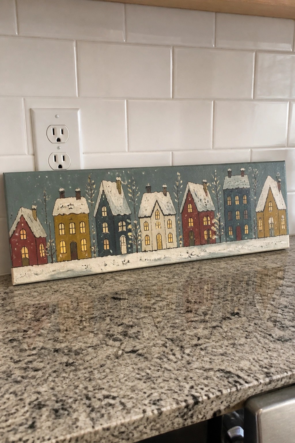 Row of colorful snow-covered houses painted on rectangular wooden sign on counter