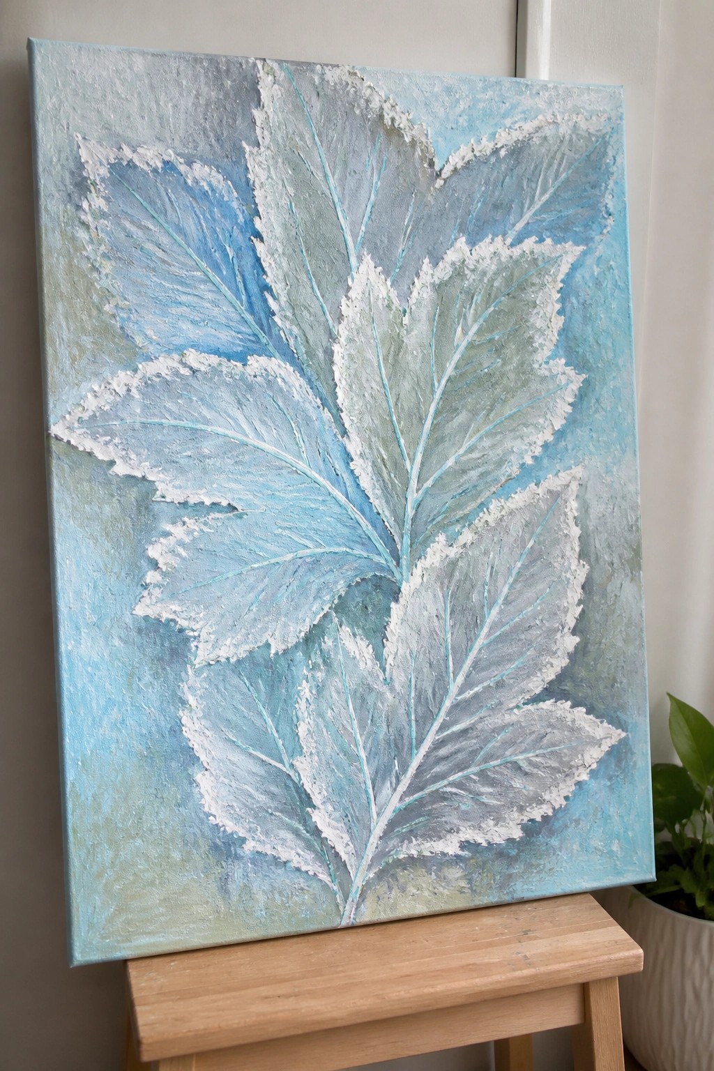 Textured blue and white leaves painting on canvas atop wooden easel.