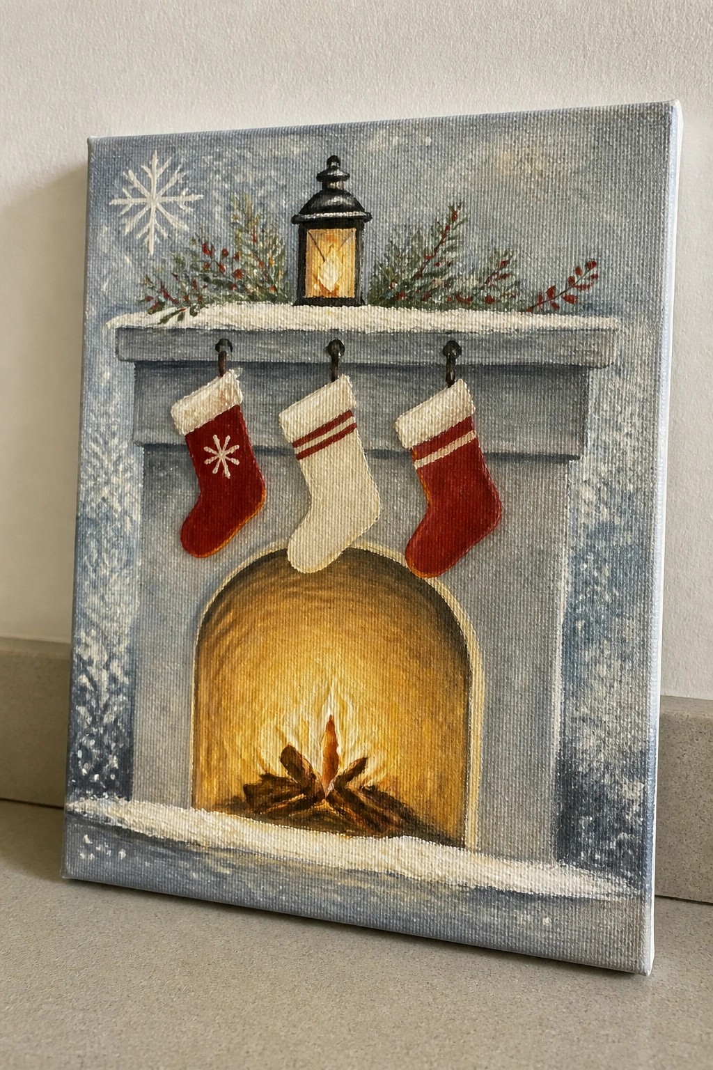 Festive fireplace painting with three stockings, glowing lantern, fire, and snow.