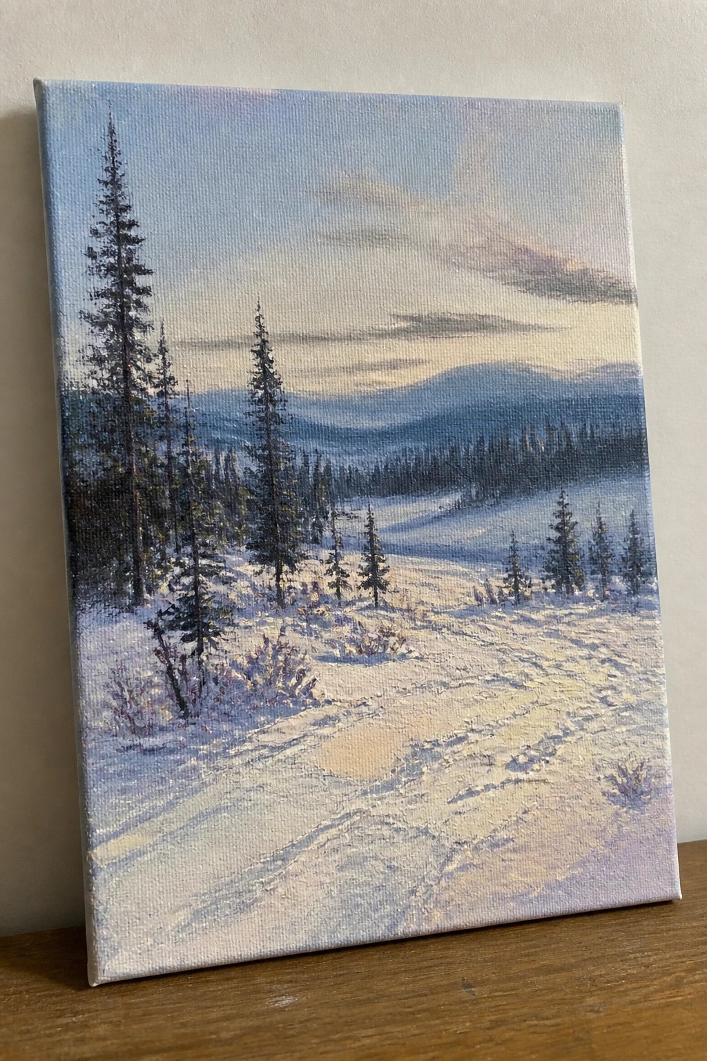 Canvas painting of snowy landscape with tall pines, hills and soft dawn sky