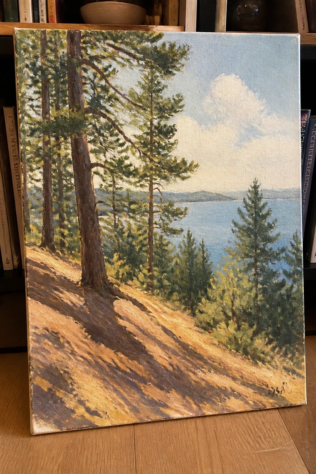 Tall pines on sunlit hillside overlooking blue lake in landscape painting on wooden floor