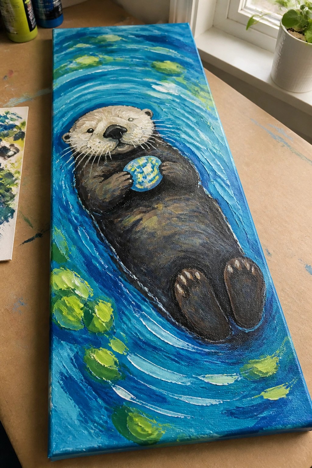 A vertical painting of a sea otter on its back in blue water holding a small ball with green shapes around it.