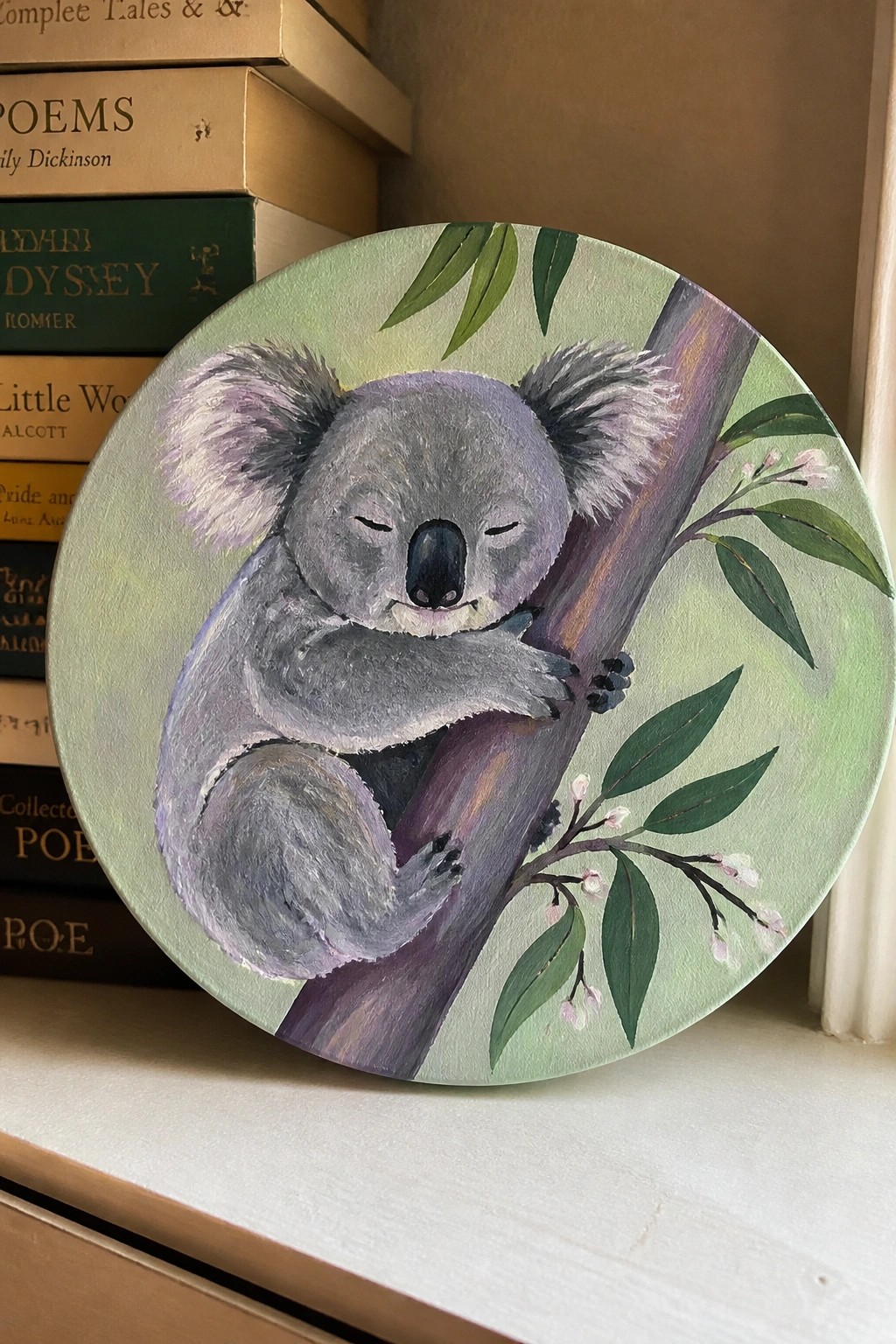 Sleeping koala painted on round green canvas beside stack of books.