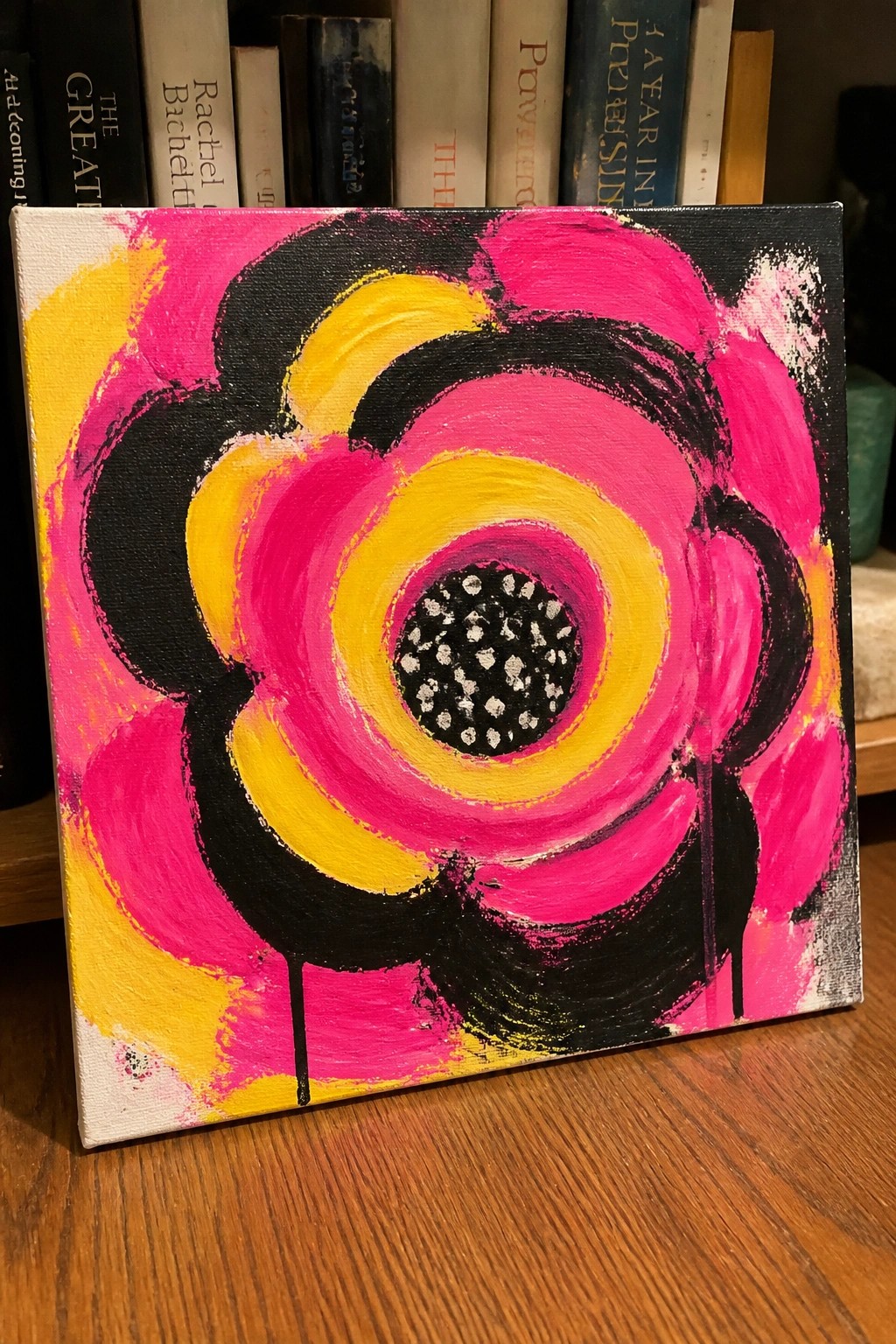 Abstract pink-yellow flower painting with black accents on canvas before books.