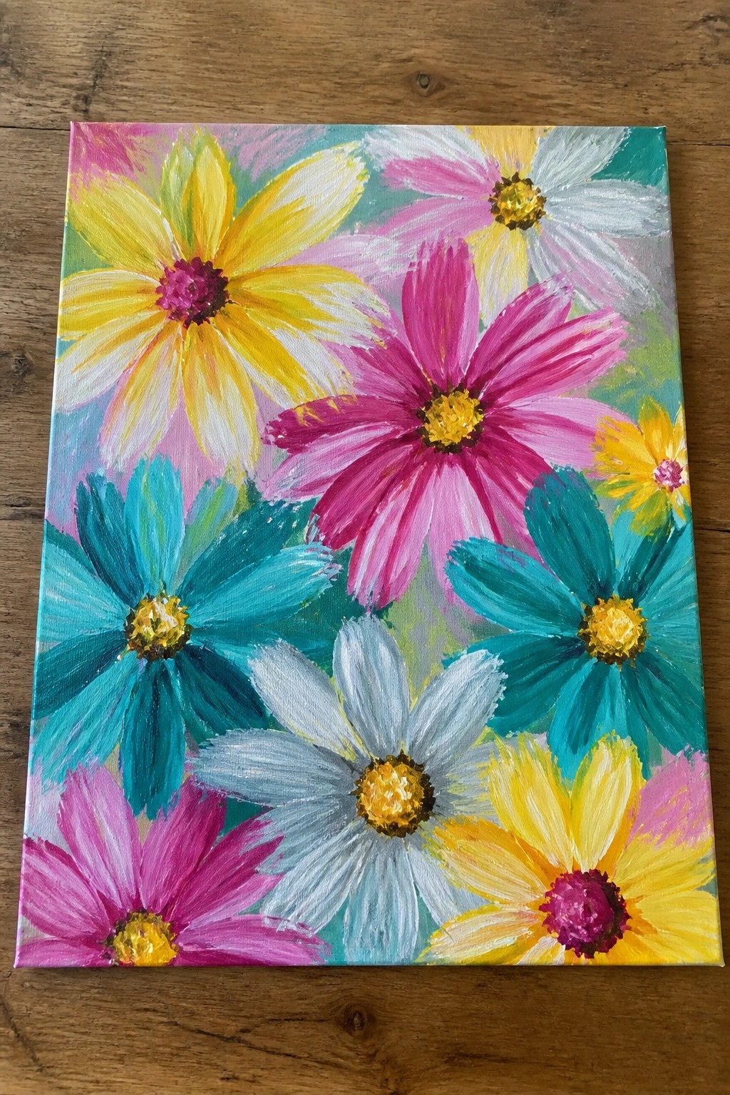 Vibrant painting of colorful daisies in yellow, pink, teal, and white on wood.