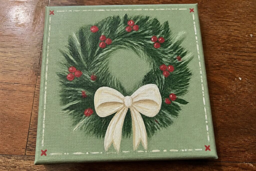 Canvas painting of Christmas wreath with green branches, red berries, and cream bow on green background.