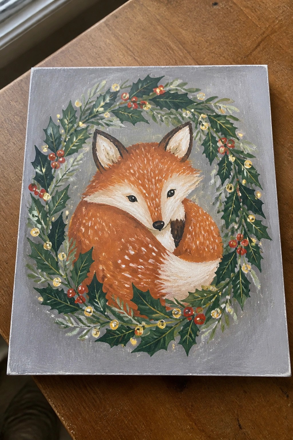 Curled orange fox inside holly wreath with red berries and glowing lights on gray canvas.