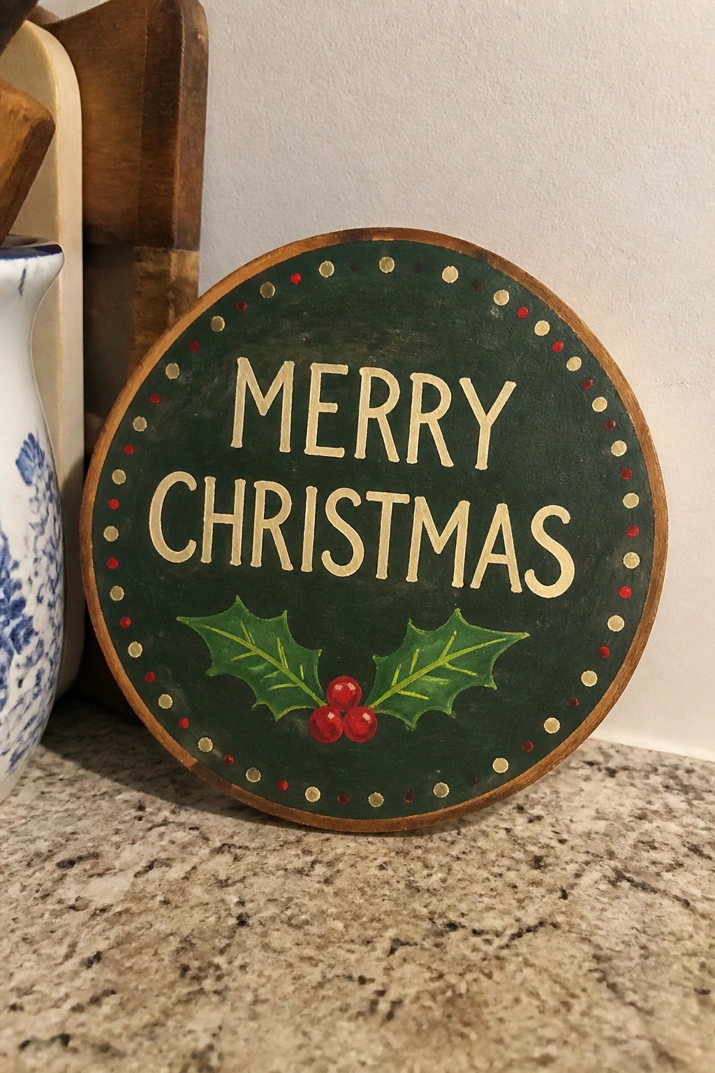 Green wooden sign with Merry Christmas text, holly leaves, red berries, and dotted border
