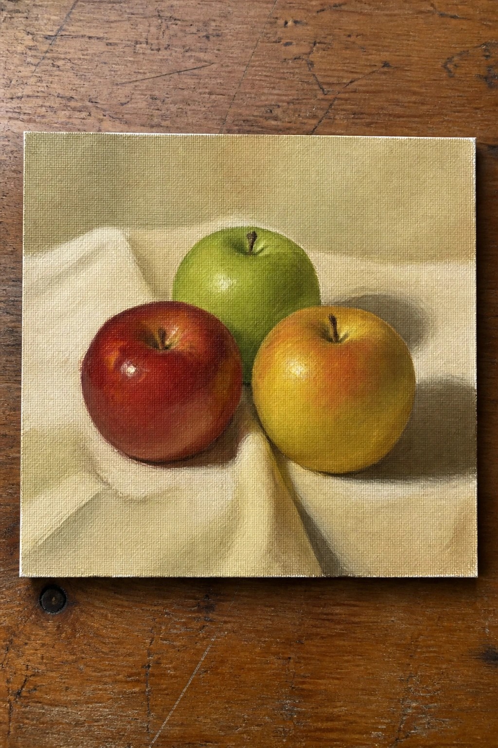 Three apples—red, green, and yellow—on white cloth over wooden surface.