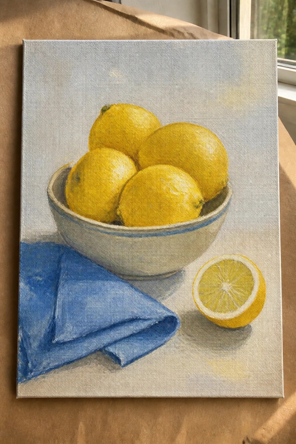 An oil painting shows whole yellow lemons in a white bowl with a blue rim, a folded blue cloth on the left, and a halved lemon on the right.