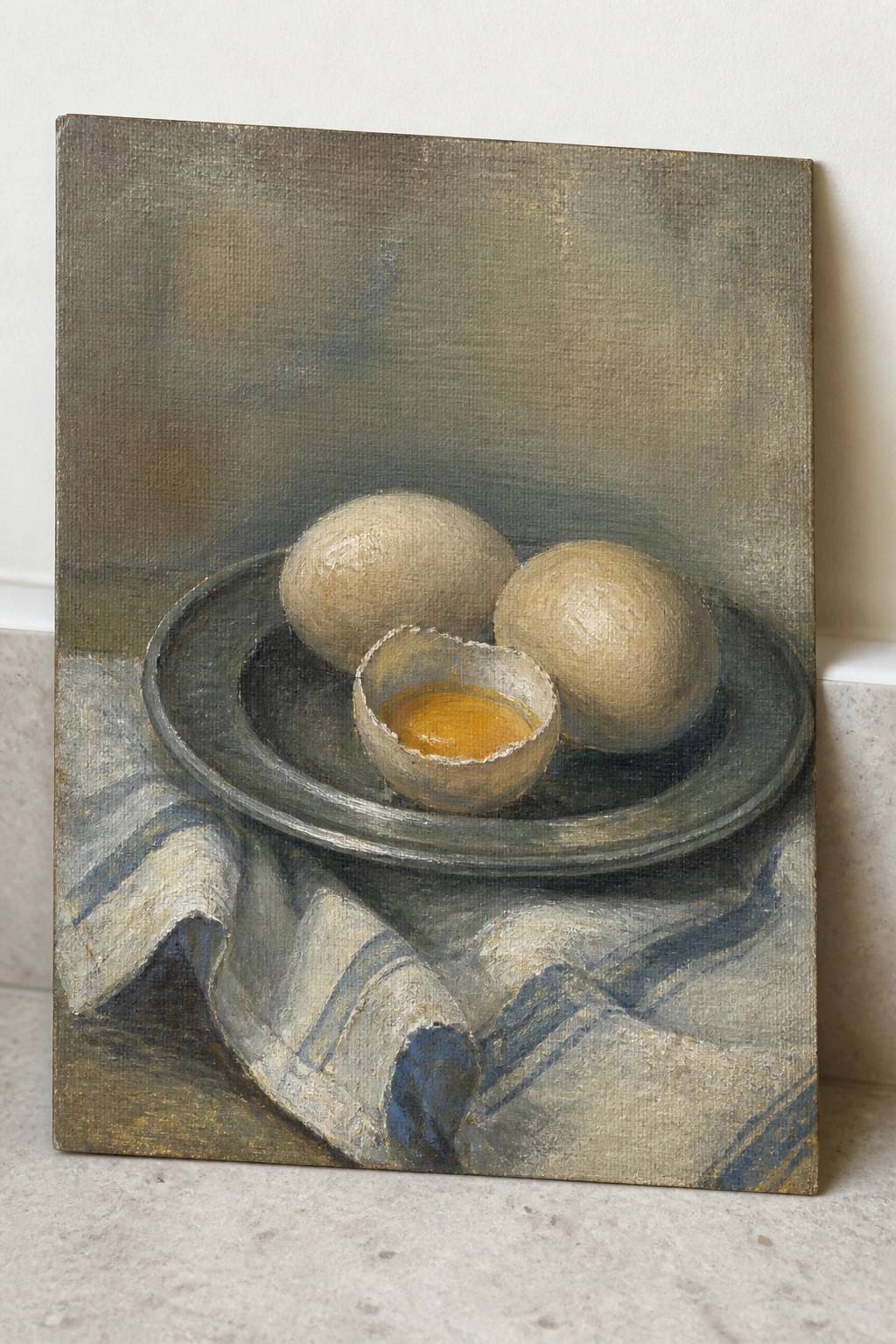 Two whole eggs and cracked shell with yolk on metal plate over blue cloth.