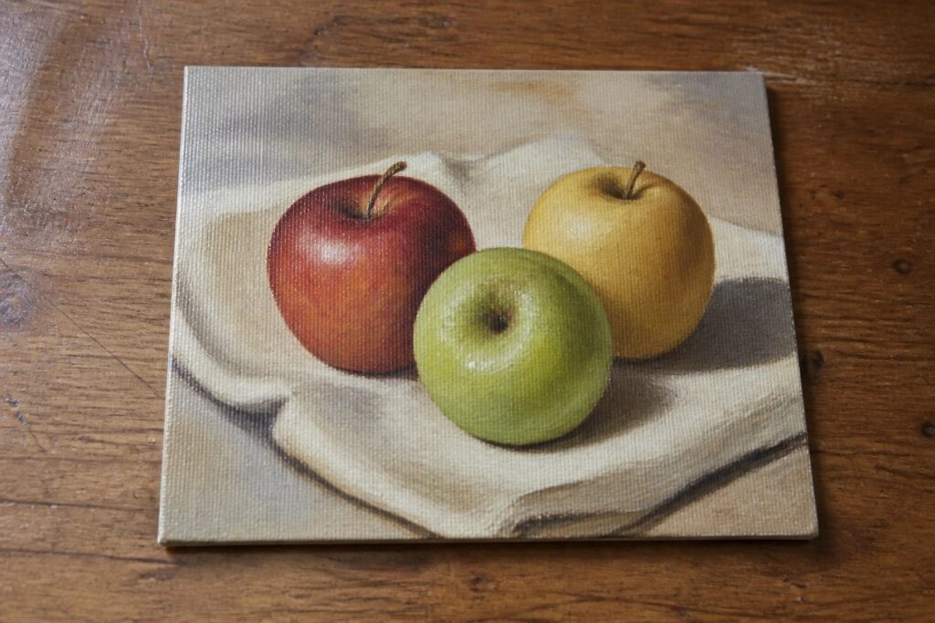 Three apples—red, green, and yellow—on white cloth over wooden surface.