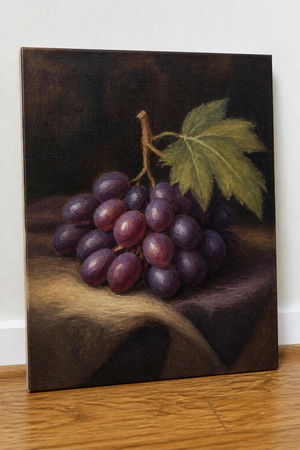 Oil painting of purple grapes with green leaf on brown draped cloth