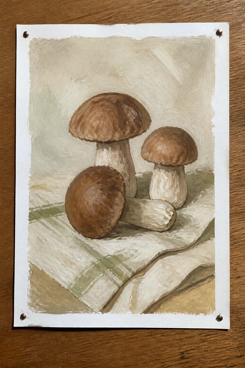 An oil painting of three brown mushrooms resting on a green and white checkered cloth against a soft beige background.