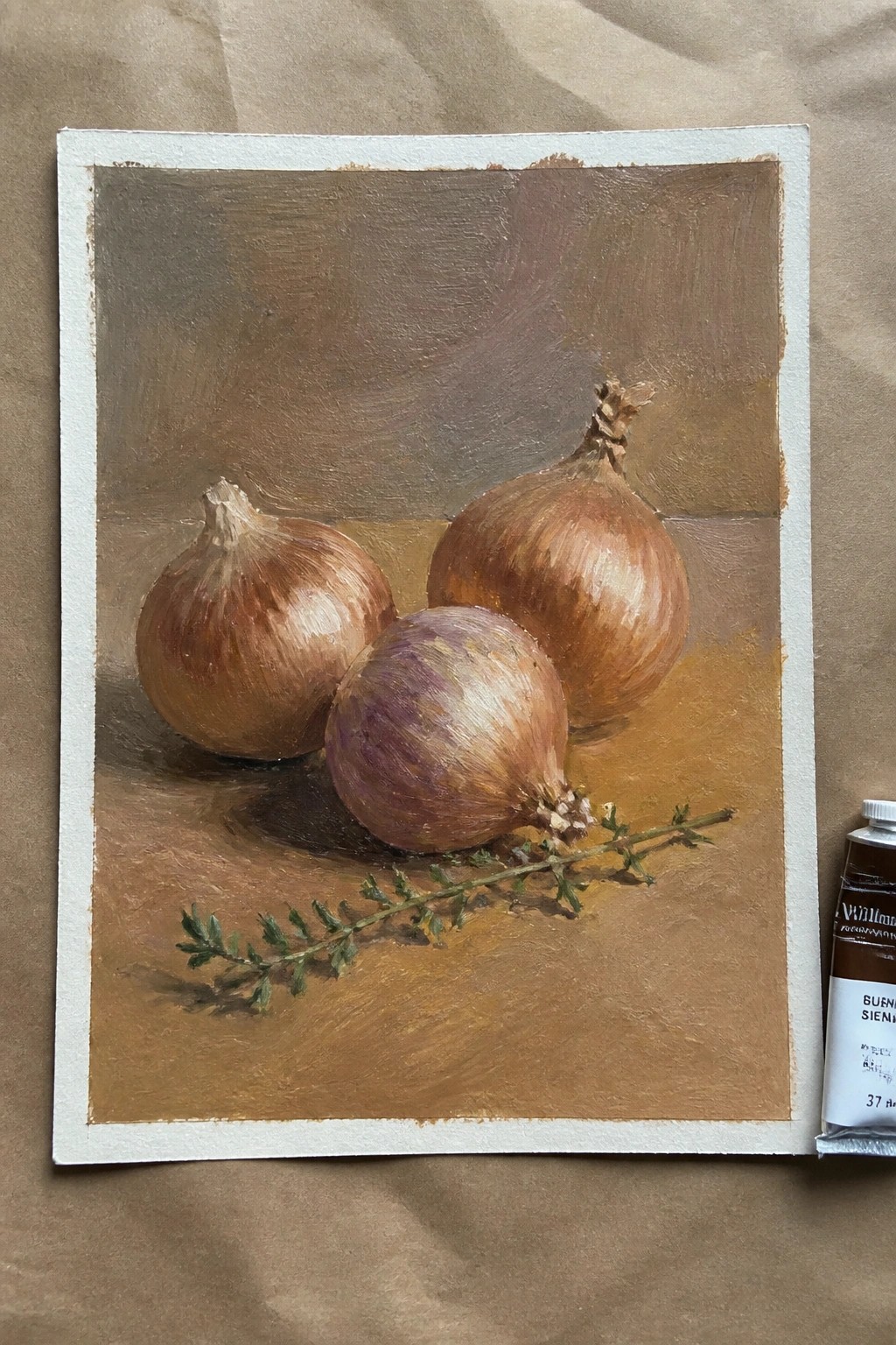 An oil painting of three onions and a sprig of thyme resting on a brown surface next to a tube of paint.