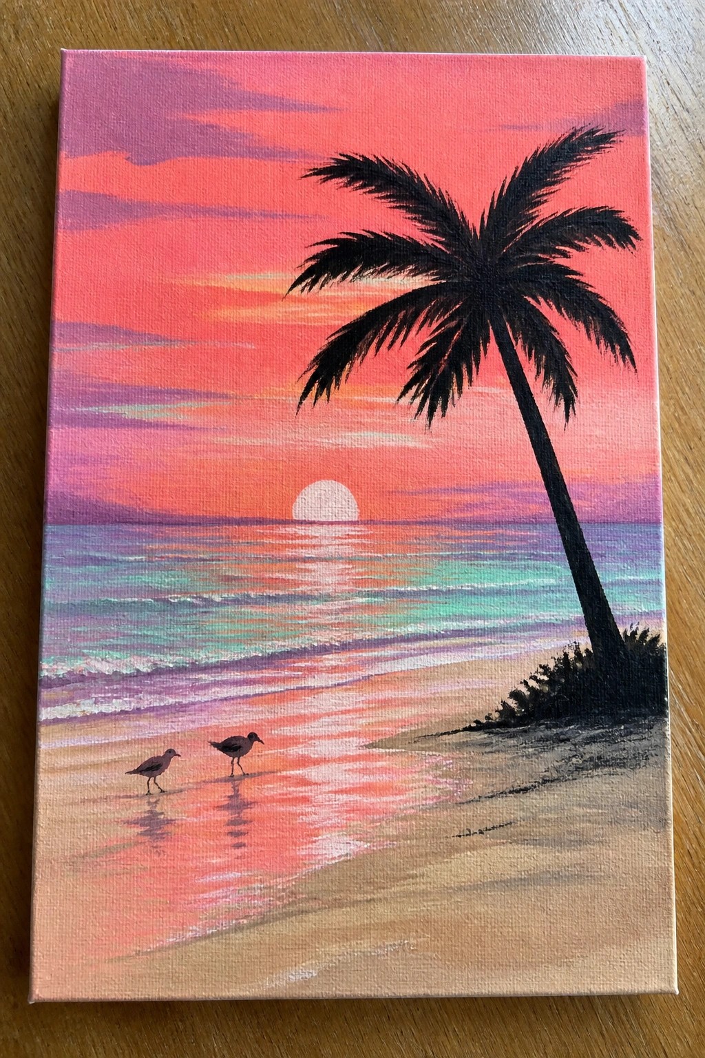 Vibrant sunset painting with pink sky, palm tree, ocean waves, sun, and two birds.