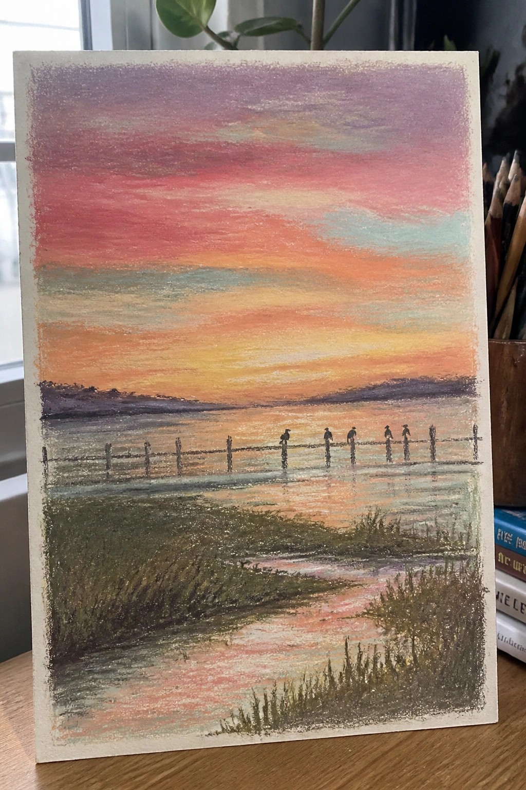 Vibrant pastel sunset over marshland with birds perched on a wooden fence.