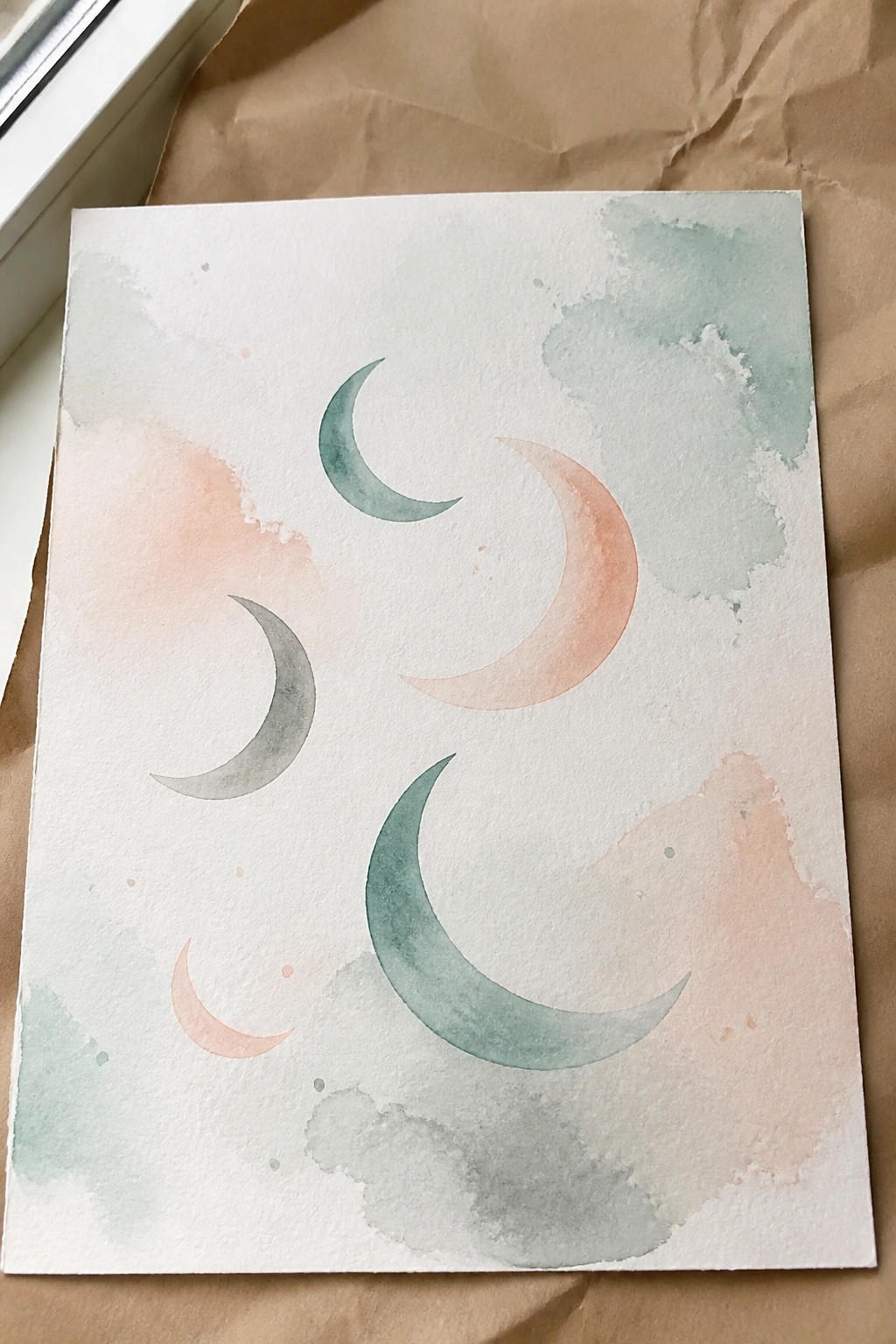 Watercolor painting of five pastel crescent moons on textured white paper with soft washes.