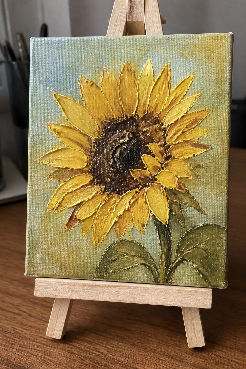 Yellow sunflower with thick yellow petals and dark center on wooden easel