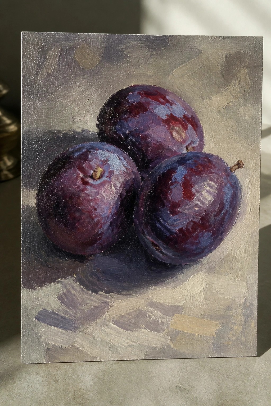 An oil painting of three dark purple plums grouped together on a gray textured background with visible brushstrokes and soft shadows.