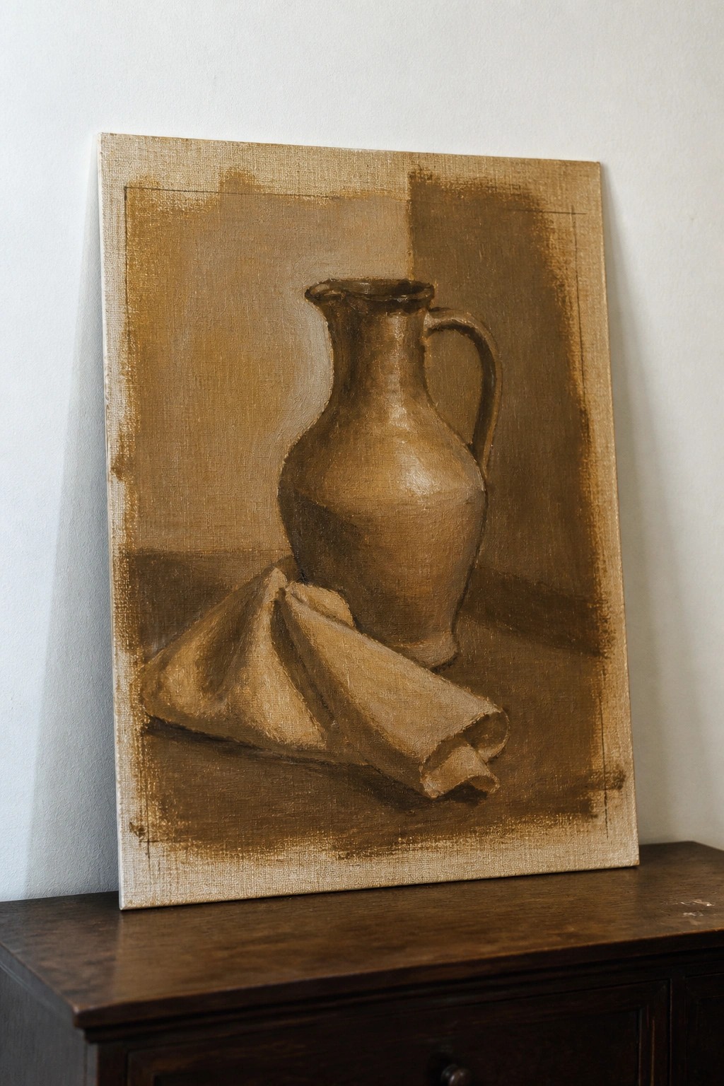 Earth-toned still life painting of pitcher beside folded cloth on canvas