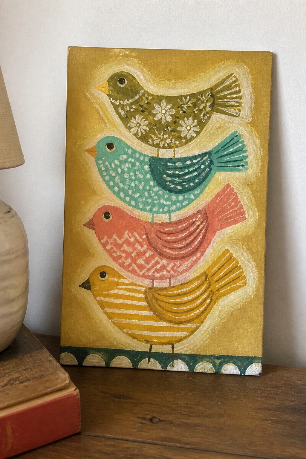 Folk art painting of four colorful stacked birds on yellow background beside lamp