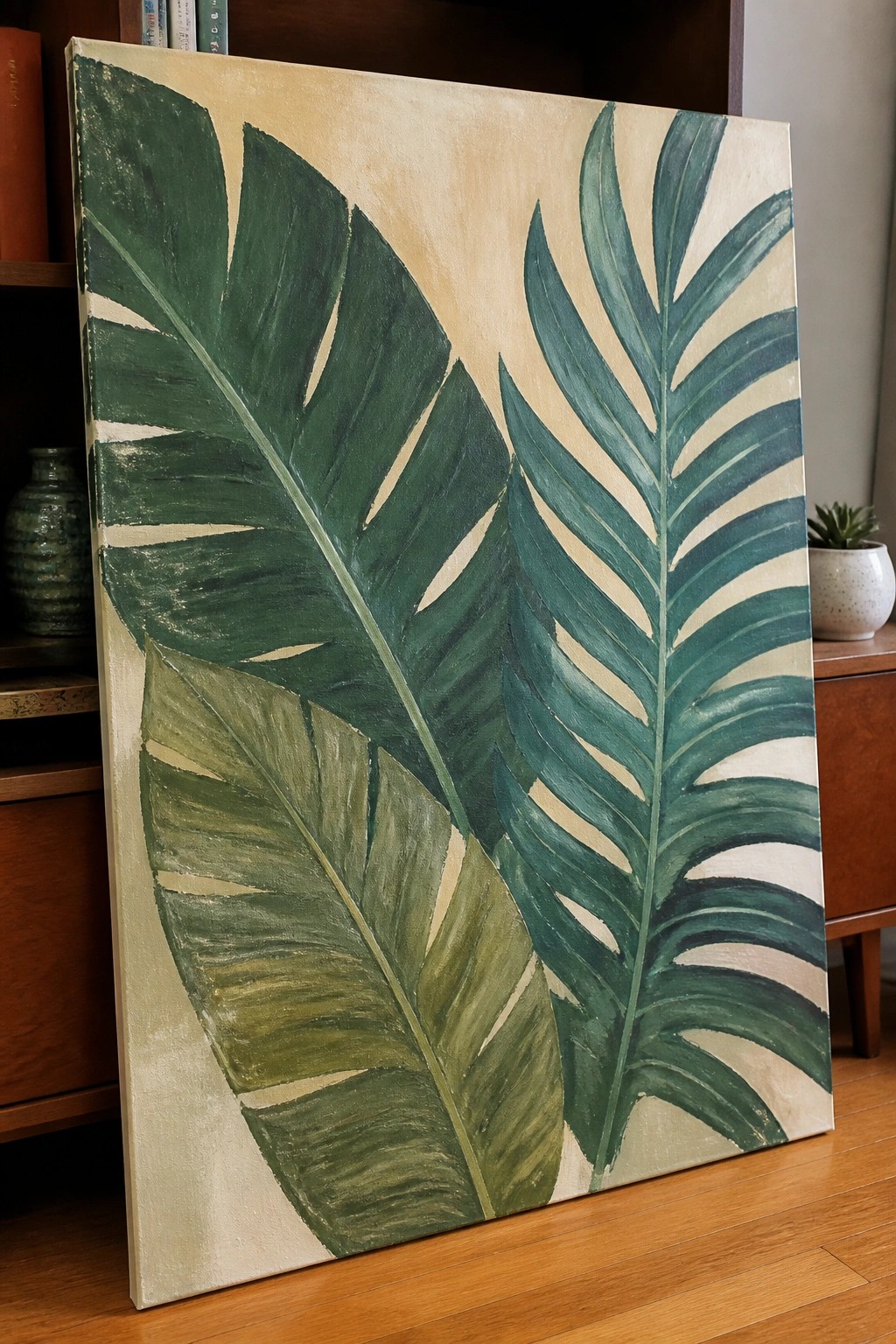 Large canvas painting of green tropical leaves on beige background in room.