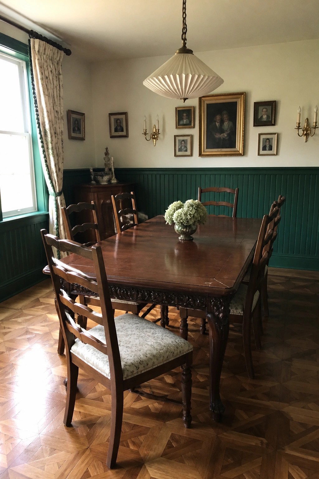 Dark wood dining table with flower vase in green wainscoted room with portraits.