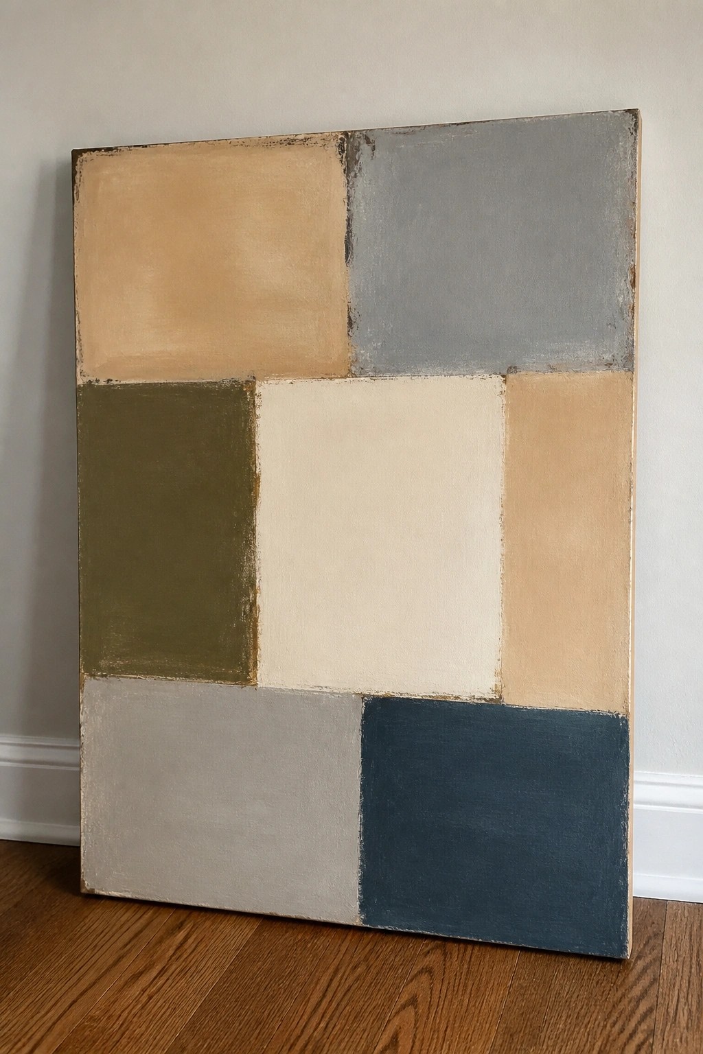 Abstract geometric painting with beige, gray, olive, cream, and blue rectangles on wooden floor.