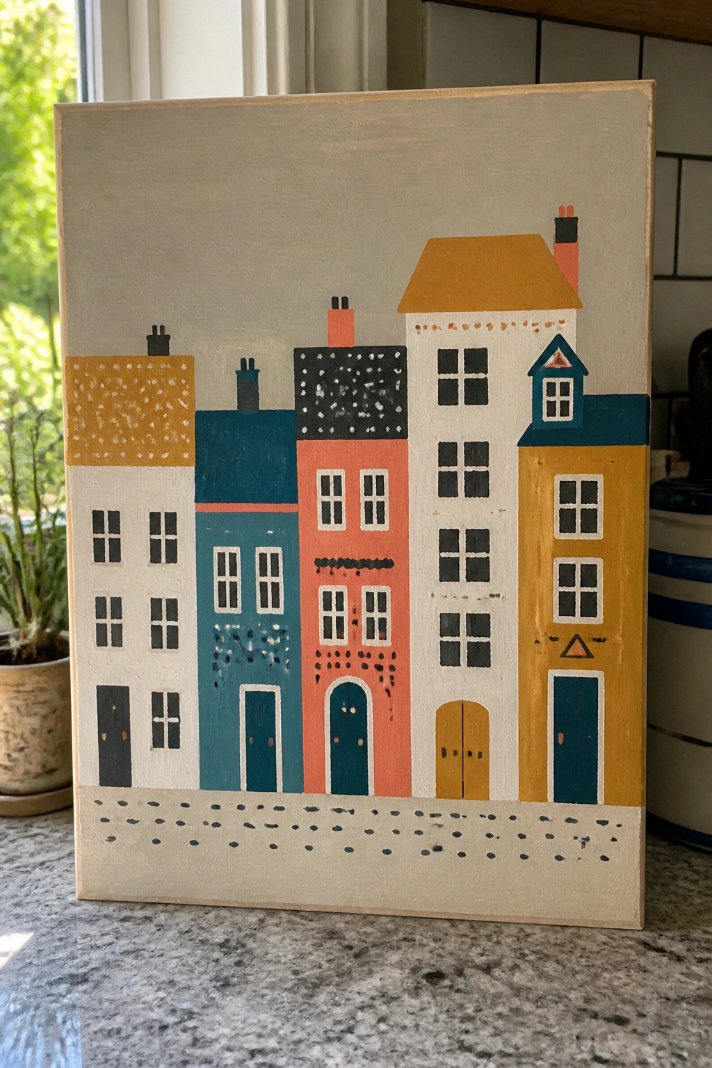 Colorful folk-art painting of row houses with bright facades, windows, doors, and chimneys on canvas.