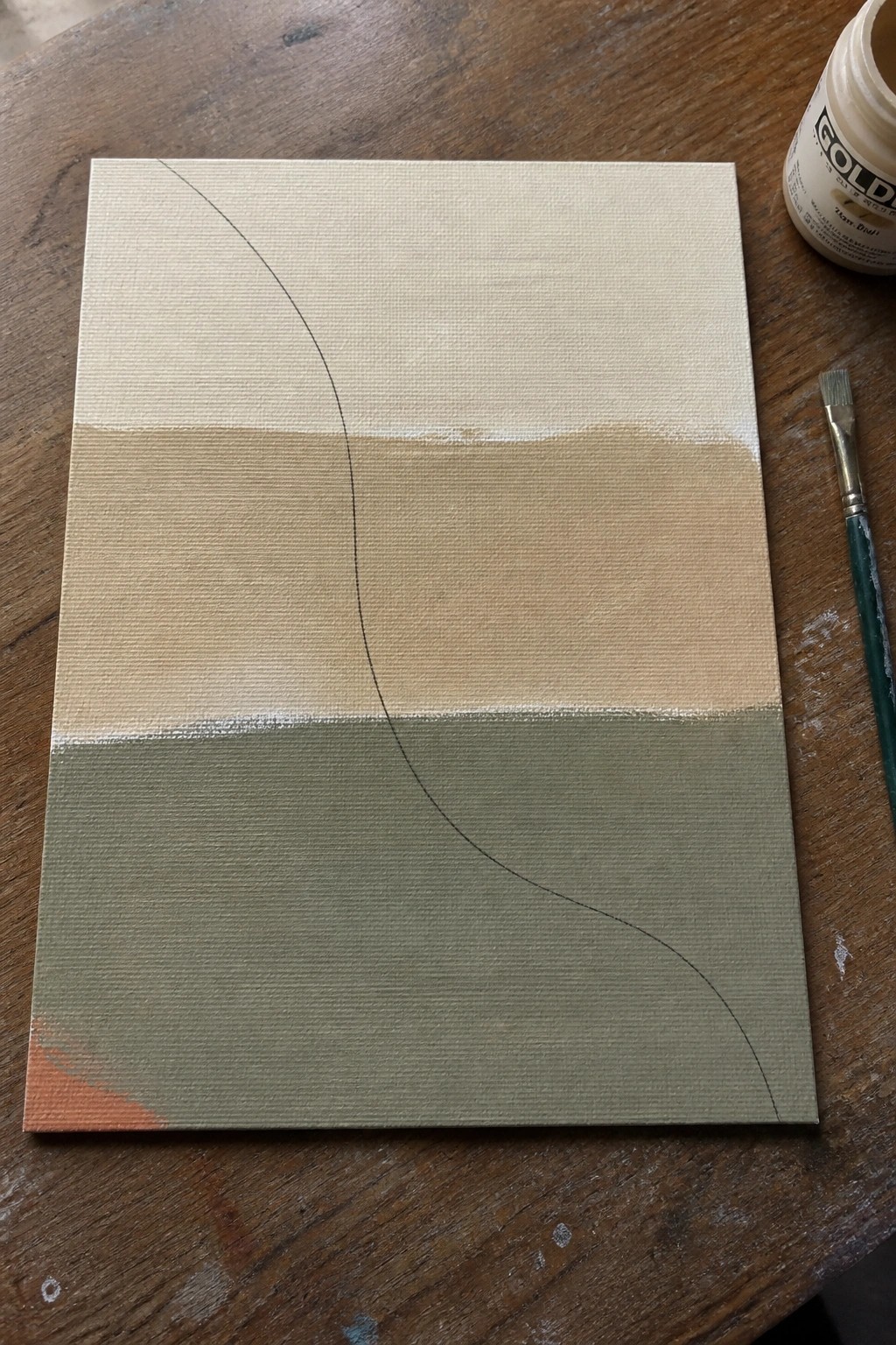 Canvas with beige-green horizontal bands, black curve, paintbrush and jar on wooden table