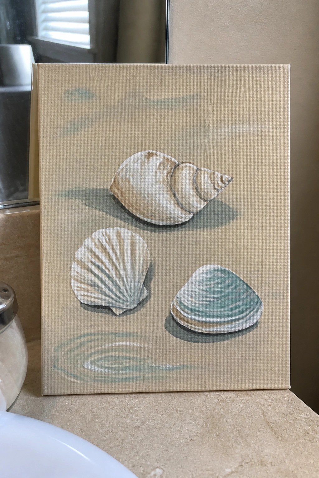 Three seashells painted on beige canvas propped on bathroom marble counter