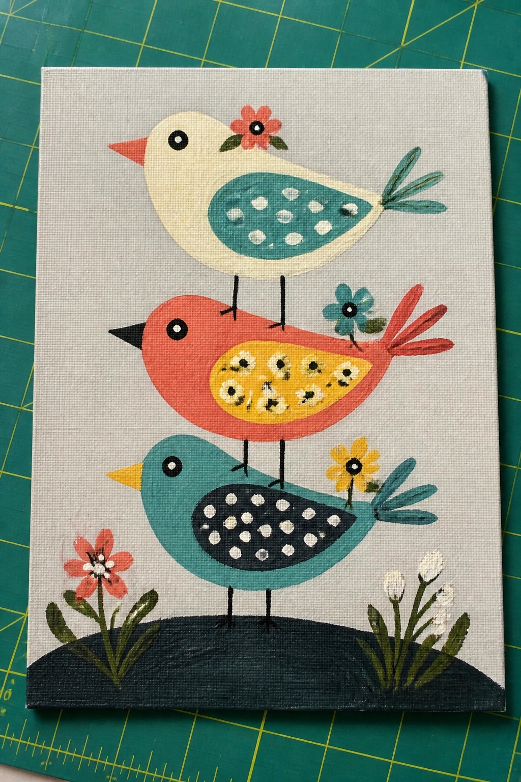 Three stacked colorful birds with patterned wings on a dark hill with flowers.