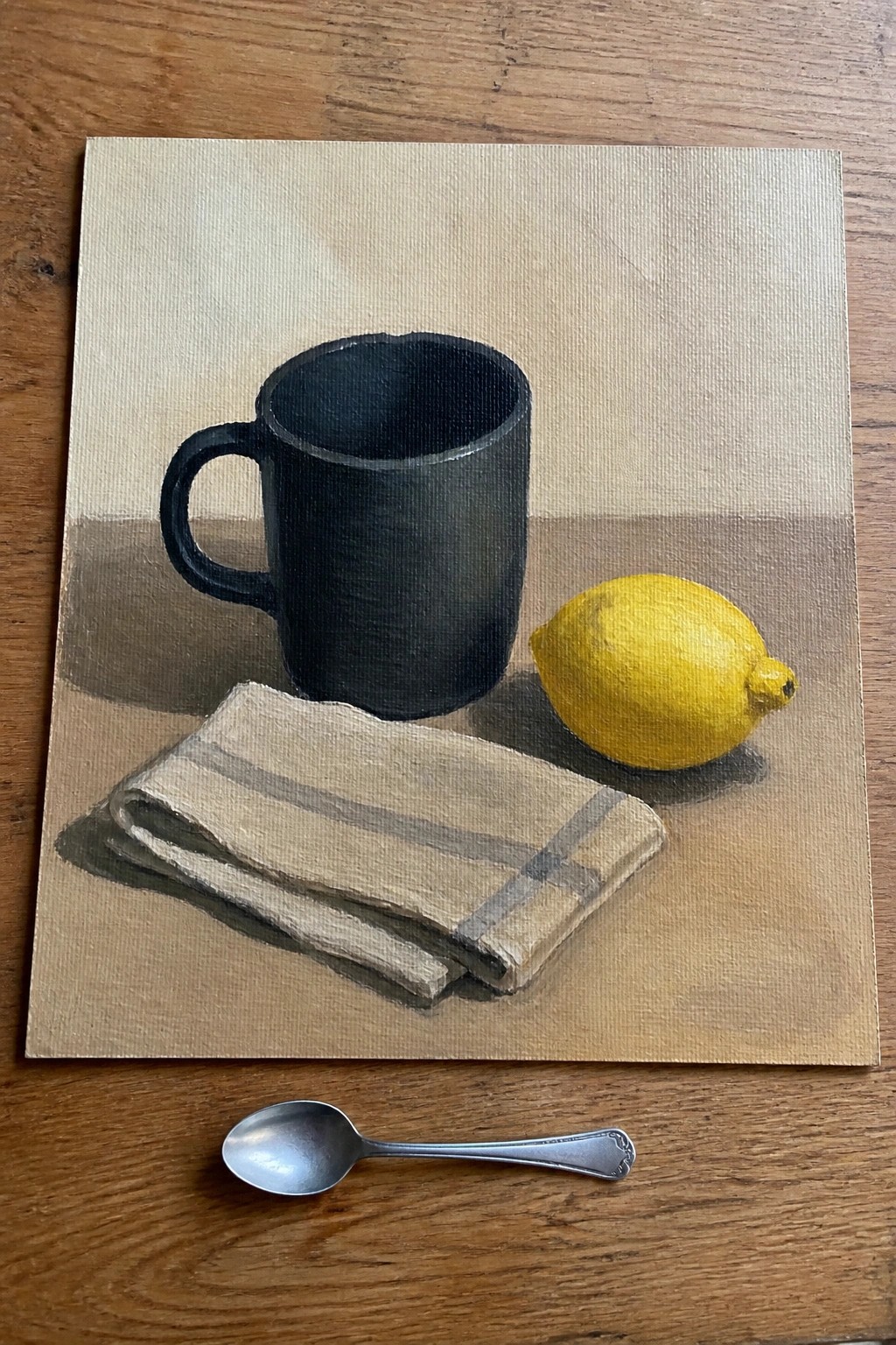 Still life painting of black mug, yellow lemon, striped cloth, and silver spoon.