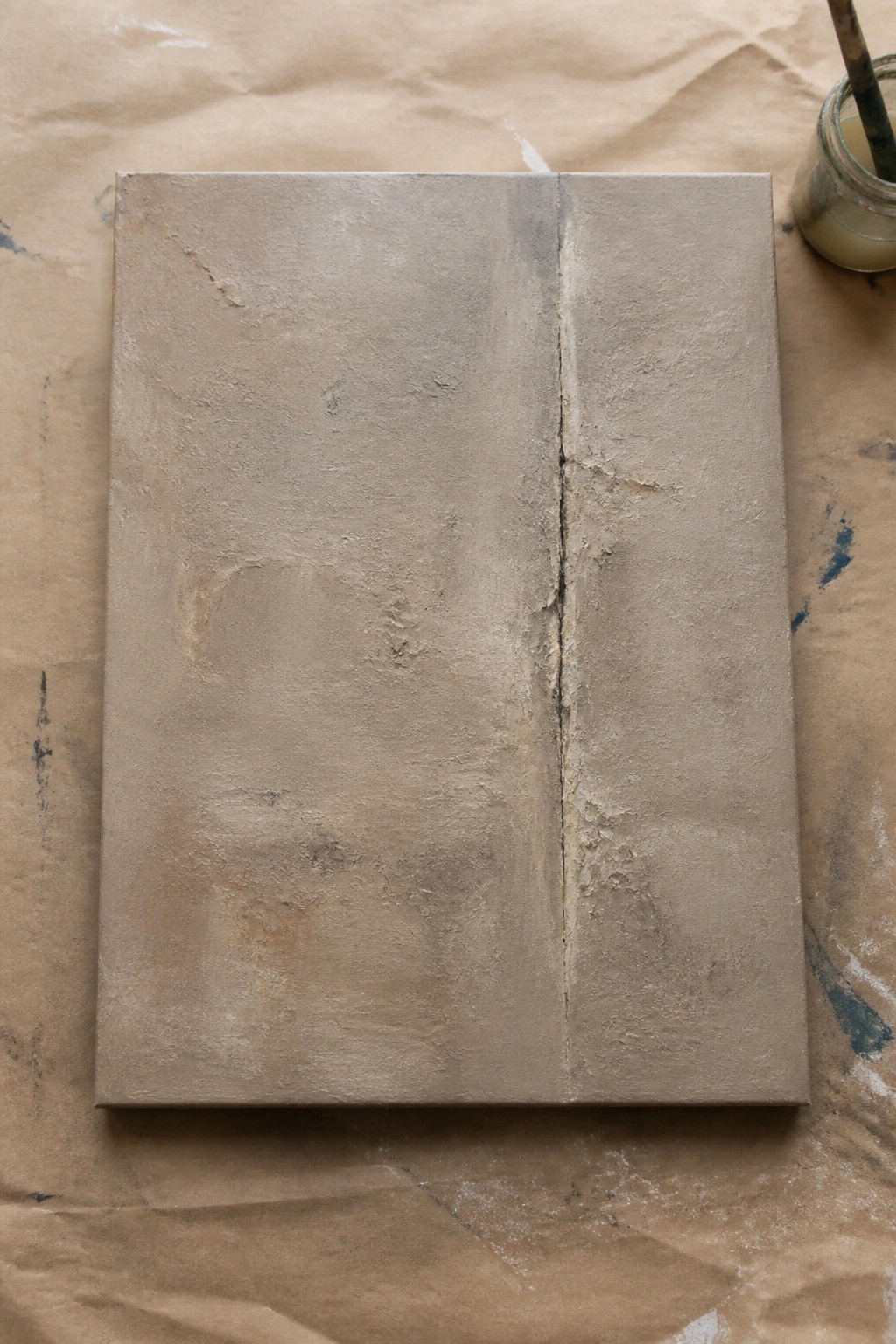 Textured beige canvas with vertical crack on brown paper beside paint jar