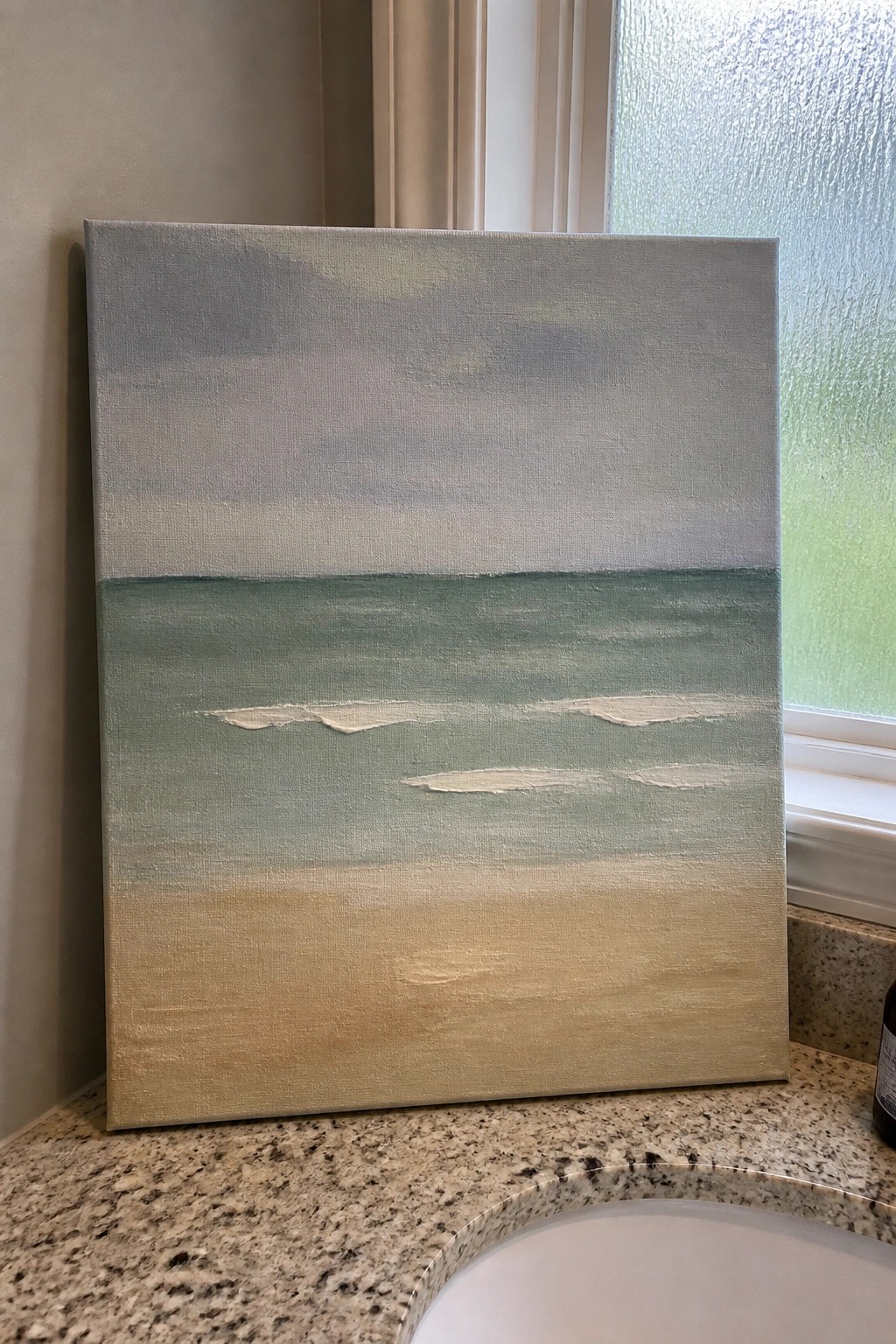 Seascape canvas with gray sky, green water with white waves, and beige sand on countertop.