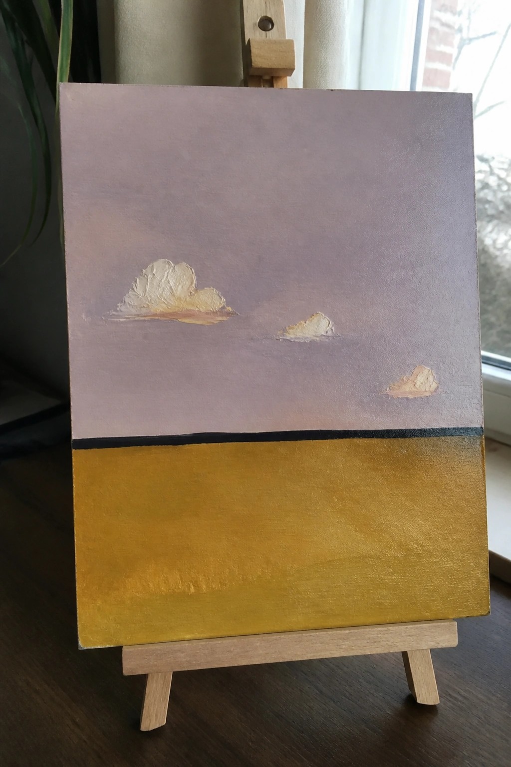 Canvas on easel with purple sky, three clouds, black line, and yellow field