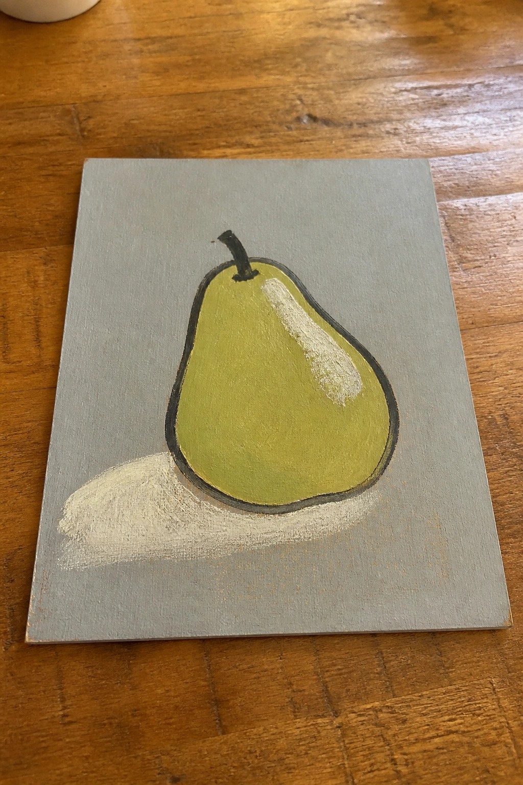 Green pear with white highlight and shadow painted on gray canvas on wood table