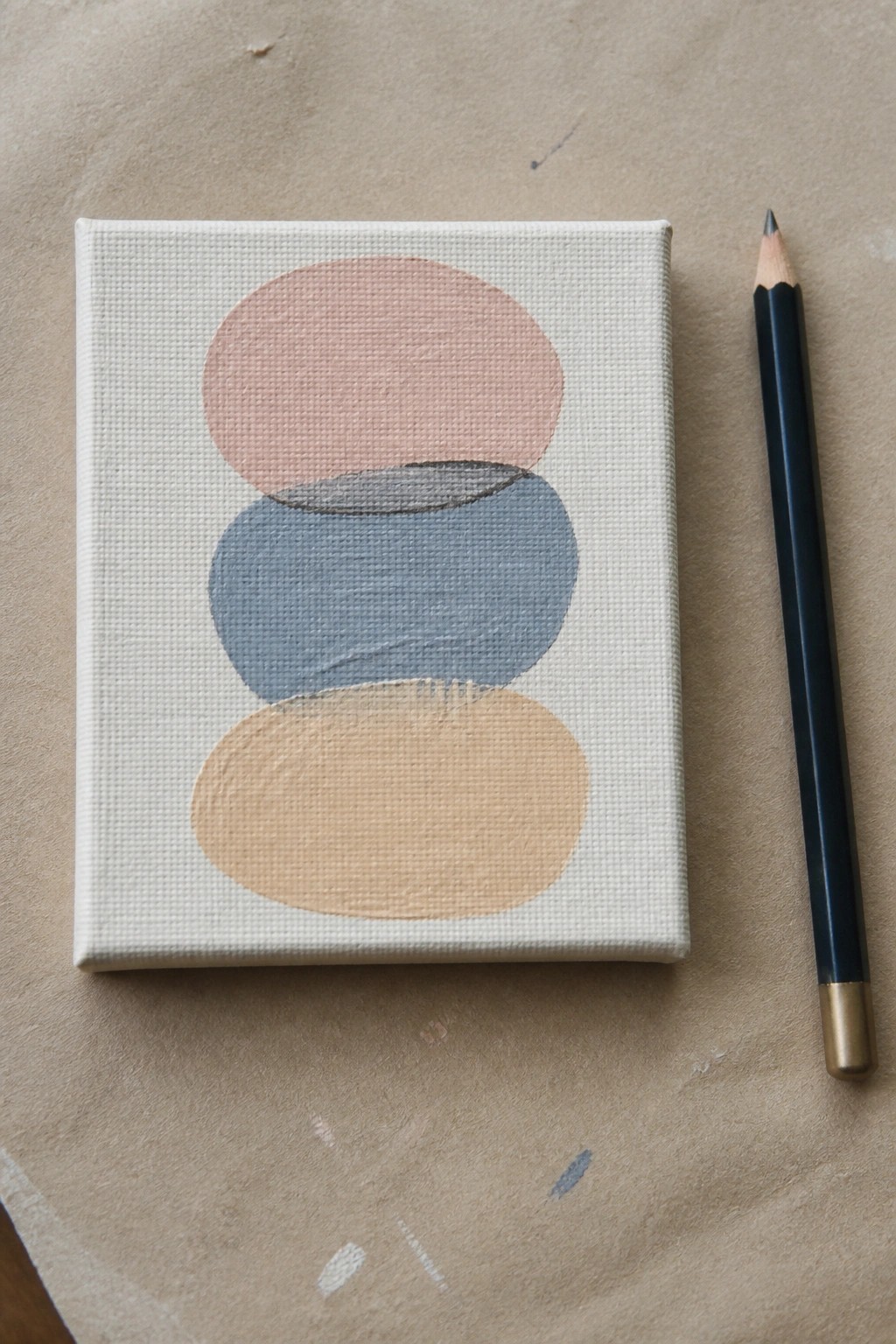 Small canvas with stacked pink, blue, and beige abstract shapes beside black pencil