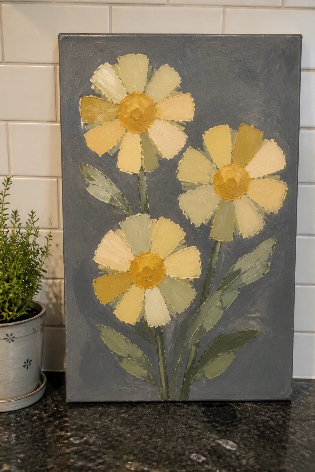 Canvas painting of three yellow-gold flowers on gray background beside potted plant.