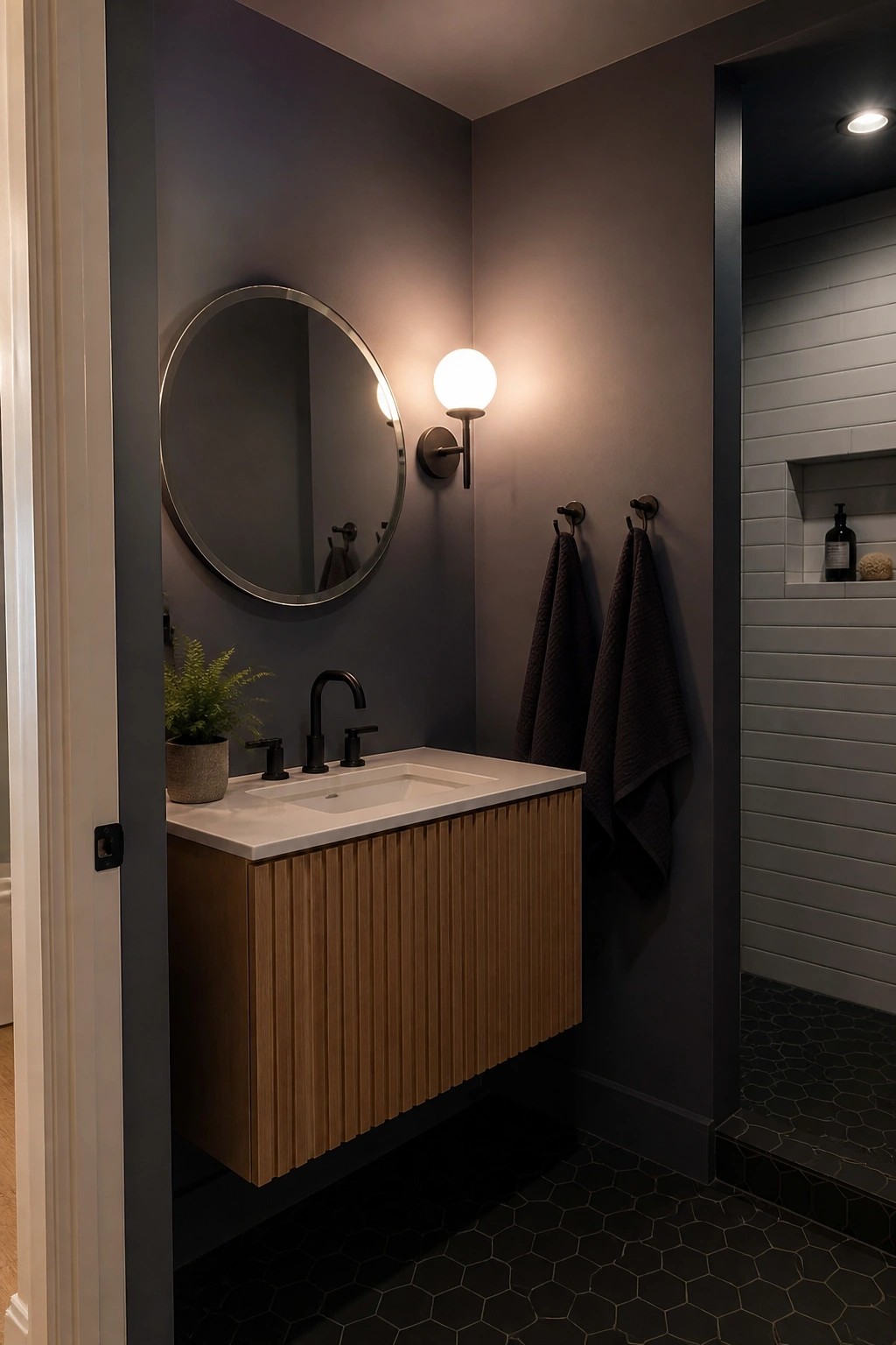 Modern bathroom with fluted wood vanity, round mirror, dark walls, and tiled shower.