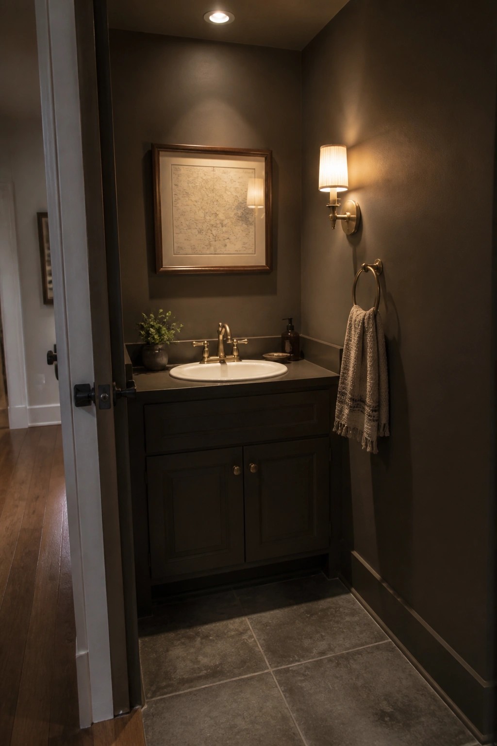 A small bathroom with deep charcoal walls, a white sink, and brass fixtures under warm evening light.