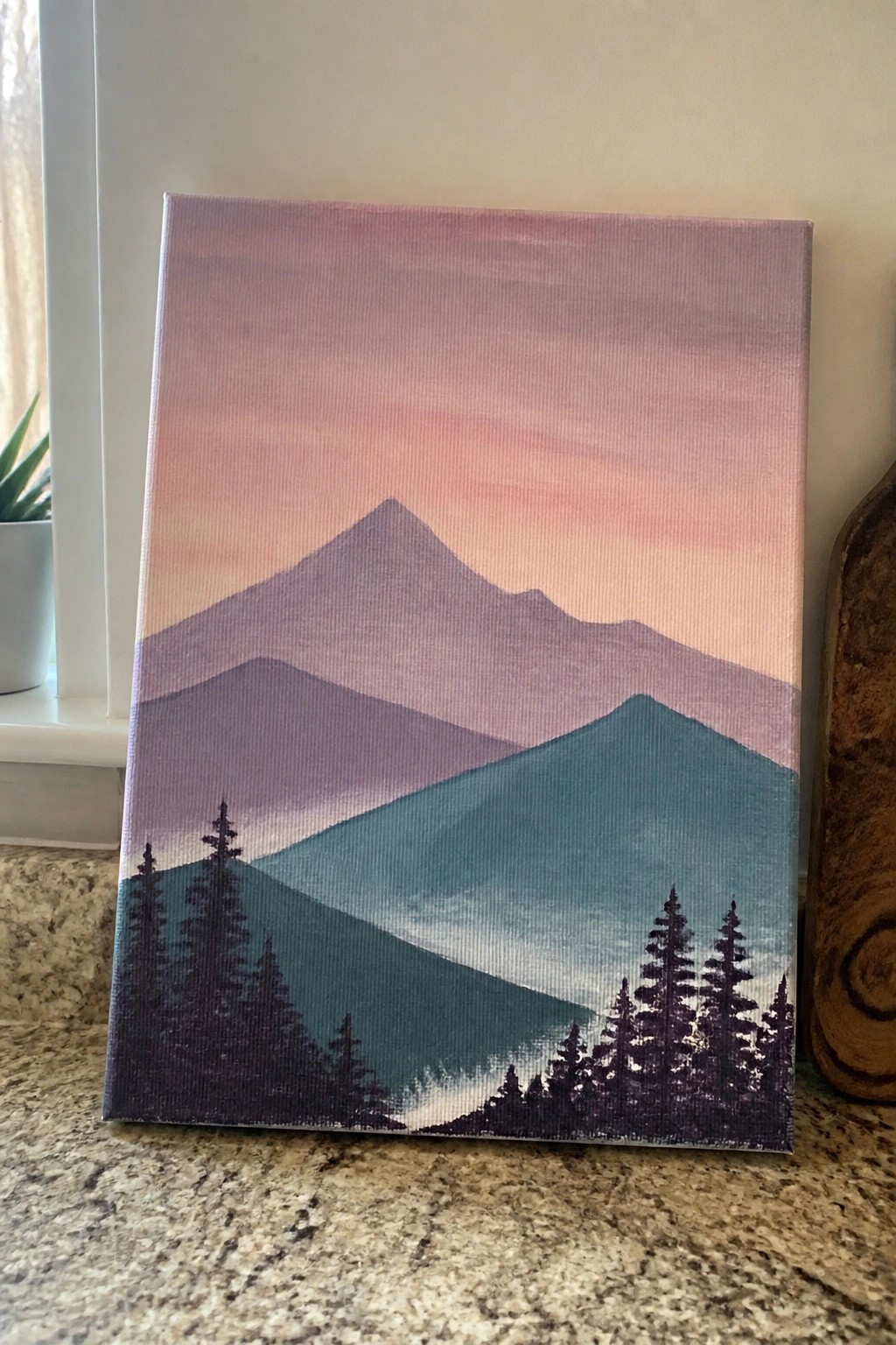 Layered purple mountains under pink sunset sky with dark pine tree silhouettes on canvas