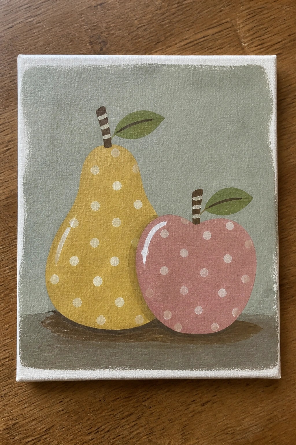 Yellow polka-dotted pear beside pink apple with striped stems on green background