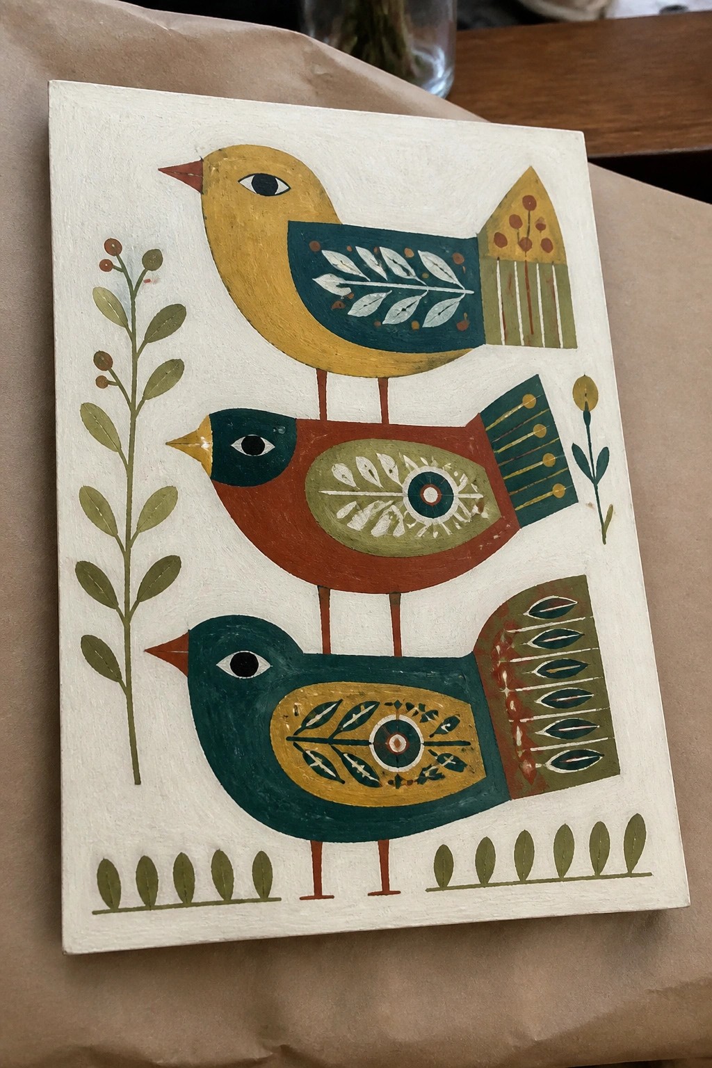 Three stacked folk-art birds in yellow, red, and teal with patterned wings and plants.