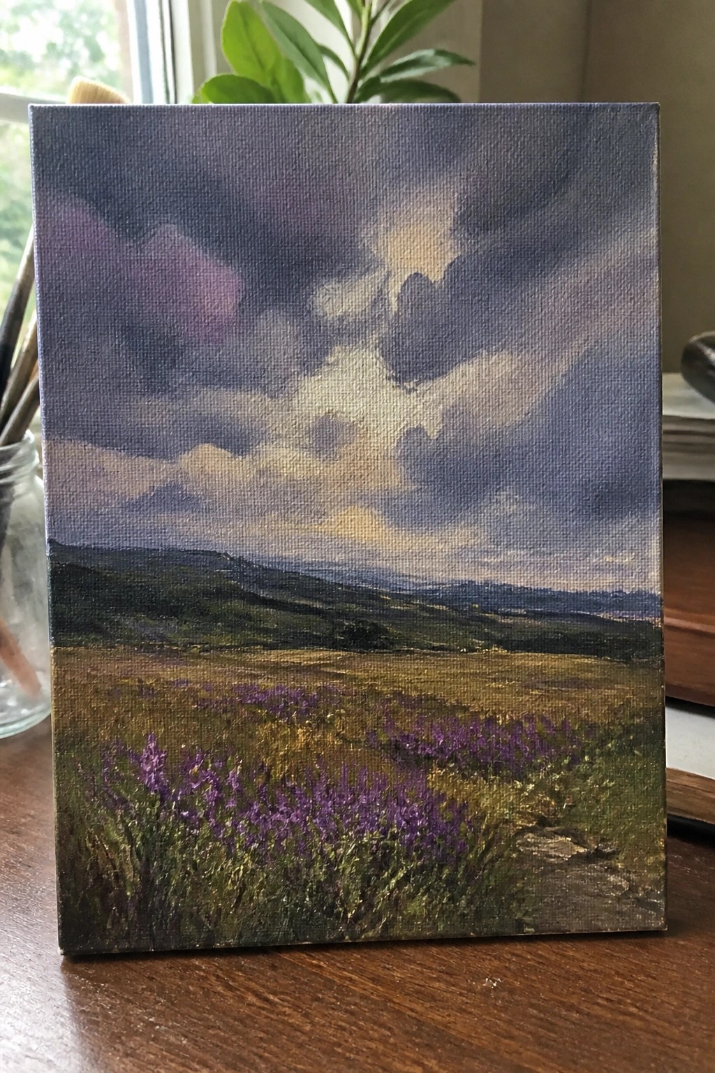 Canvas painting of stormy purple sky over green hills and purple wildflower field.