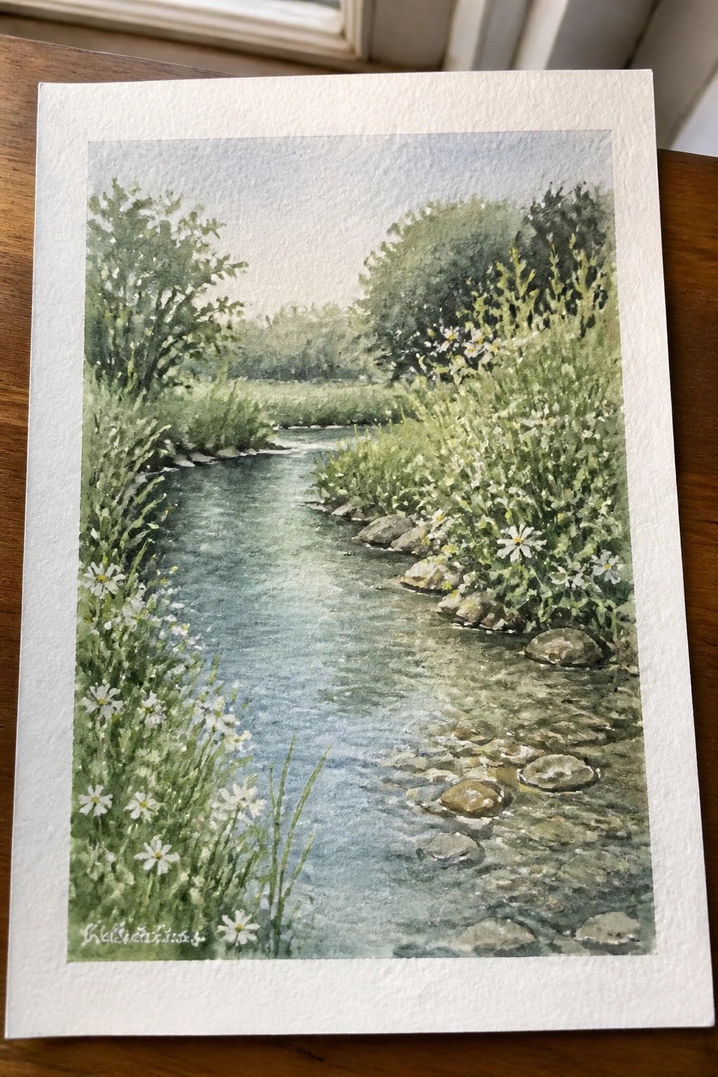 Watercolor painting of a winding stream with stepping stones amid green bushes and white flowers.