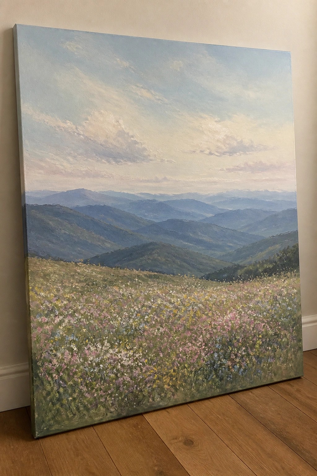 Large impressionistic painting of wildflower meadow with layered blue mountains on wooden floor