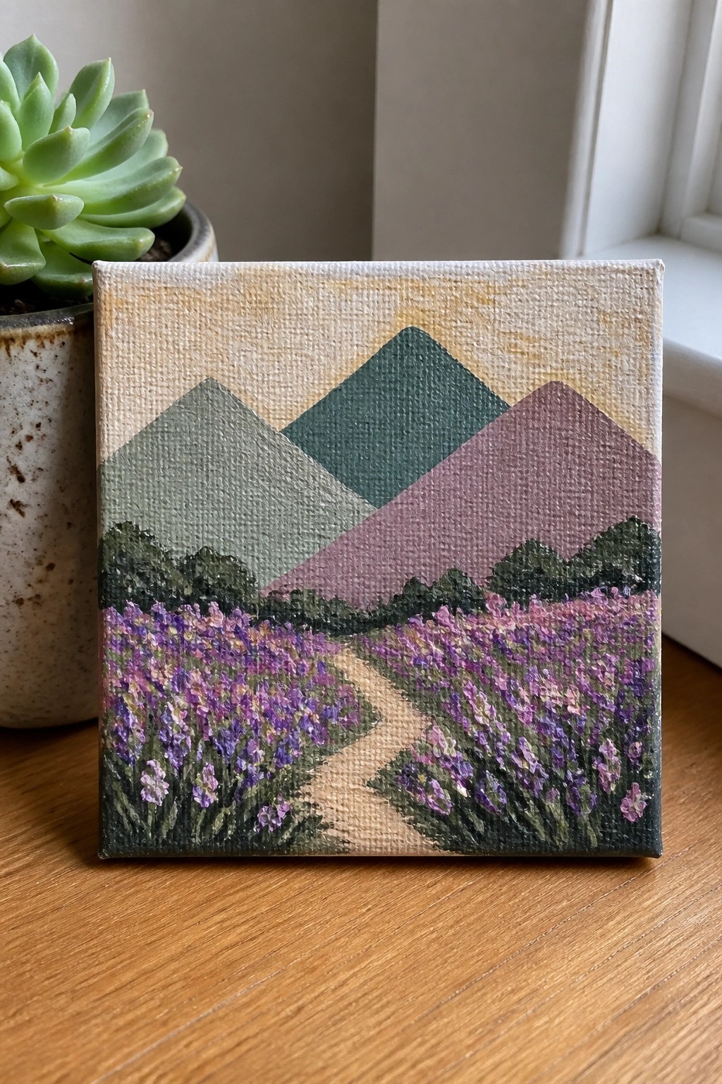 Small painting of lavender fields and mountains beside potted succulent on wood.